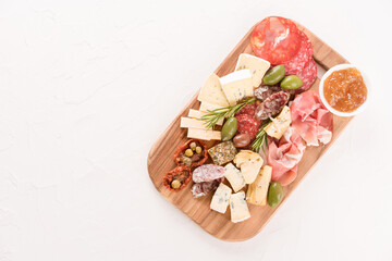 Italian antipasti board with variety of cheeses, sausages served with sun dried tomatoes, olives, jams at white table - parmesan, dorblu, prosciutto. Cheese and meat snacks platter.  Copy space