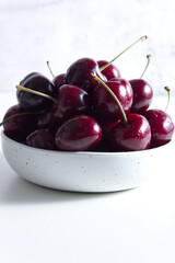 Red juicy cherries in a white ceramic bowl on a light background