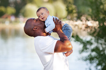 African American father kisses, holds on arms and loves child son mixed race outdoors in summer