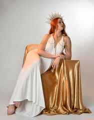 Full length portrait of beautiful red head woman wearing long flowing fantasy toga gown with golden...