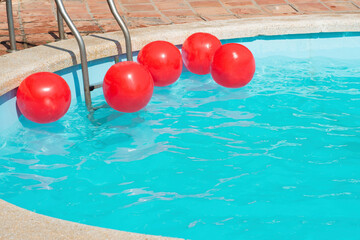 Fototapeta na wymiar bright red inflatable balls float on the surface of the laurel water in the pool in the sun