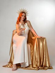 Full length portrait of beautiful red head woman wearing long flowing fantasy toga gown with golden...