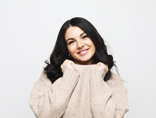 Young cute smiling brunette woman wearing casual sweater over grey background.