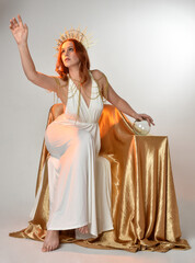 Full length portrait of beautiful red head woman wearing long flowing fantasy toga gown with golden...