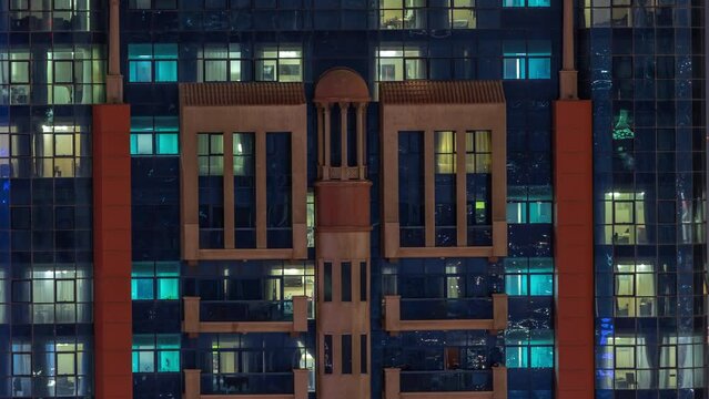 Night aerial view of apartment building glass window facade with illuminated lighted workspace rooms timelapse. Glowing light in skyscraper