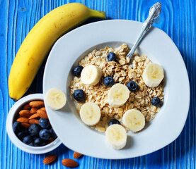 oatmeal with fresh berries, bananas on white plate with orange juice and milk, blue wooden background.