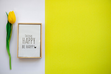 Motivational words of wish in a frame,think happy be happy on white yellow spring color tulips