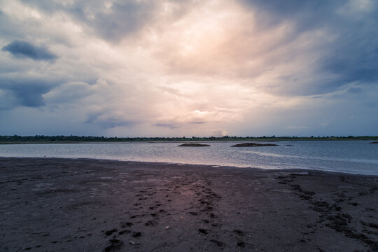 Evening sunset at the lake in Maharashtra, India. Wet muddy soil with footprints by the lake shore.