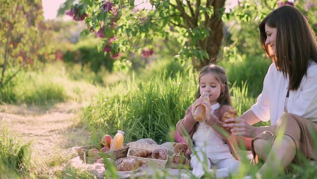 Mom and daughter on a picnic. Little girl drinks juice from a bottle.