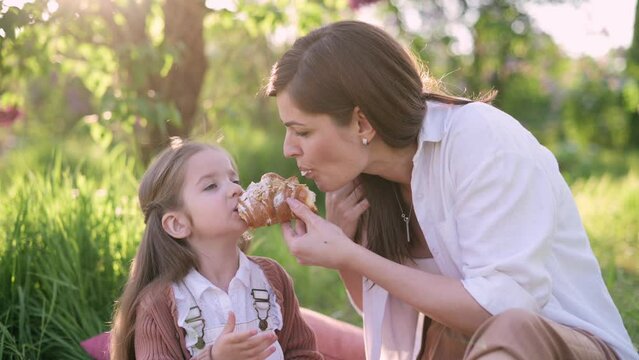 Mom and daughter on a picnic. Mom treats her little daughter with a croissant.