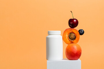 White bottle of multivitamin supplement with fresh fruits on cube stand, orange background, copy...