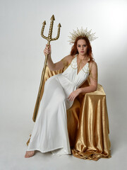 Full length portrait of beautiful red head woman wearing long flowing fantasy toga gown with golden...