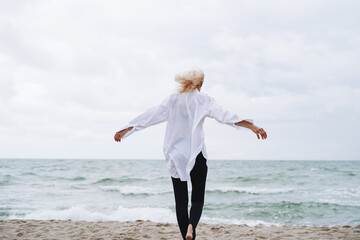 Portrait of Elegant blonde woman in white shirt on sand beach at storm sea at windy weater