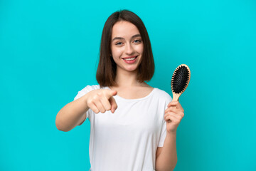 Young ukrainian woman with hair comb isolated on blue background points finger at you with a confident expression