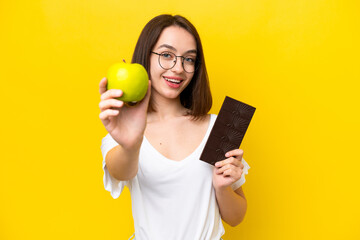 Young Ukrainian woman isolated on yellow background taking a chocolate tablet in one hand and an...
