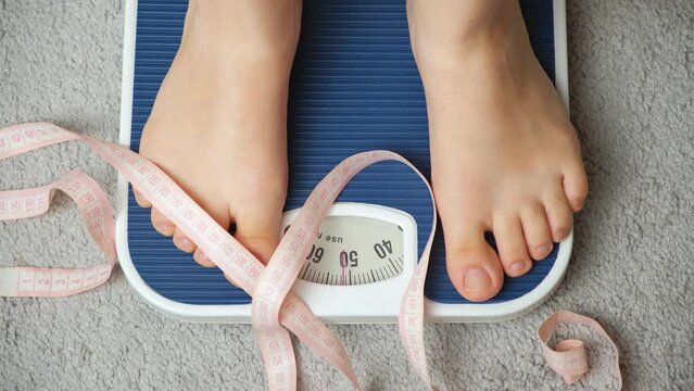A woman stands on the scales, her legs close-up, the measuring tape falls.