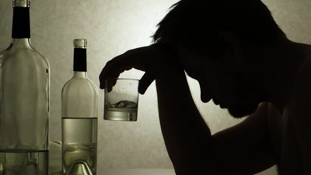 A drunk man holds a glass of alcohol sitting at a table. Alcoholism