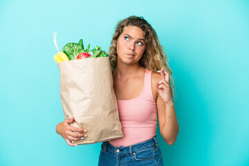 Girl with curly hair holding a grocery shopping bag isolated on green background with fingers crossing and wishing the best