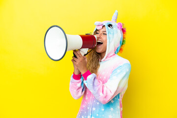 Girl with curly hair wearing a unicorn pajama isolated on yellow background shouting through a megaphone © luismolinero