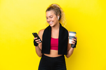 Sport woman with towel isolated on yellow background holding coffee to take away and a mobile