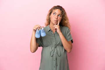 Girl with curly hair isolated on pink background pregnant and holding baby booties