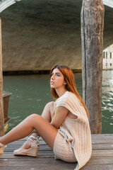 dreamy redhead woman sitting on pier in Venice and looking away.