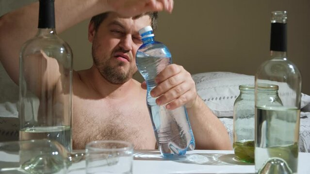 A man with an alcohol addiction in a hangover drinks mineral water