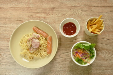 fried spicy spaghetti carbonara topping bacon with pork sausage on plate and French fries couple salad 