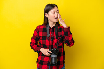Young photographer Chinese woman isolated on yellow background yawning and covering wide open mouth with hand