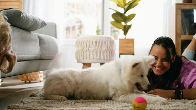 Cheerful young woman lying on the floor playing with her little dog at home