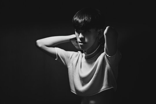 Black and white photo of Asian gay teenager with crop-top shirt putting a necklace, People lifestyle fashion LGBTQ concept.
