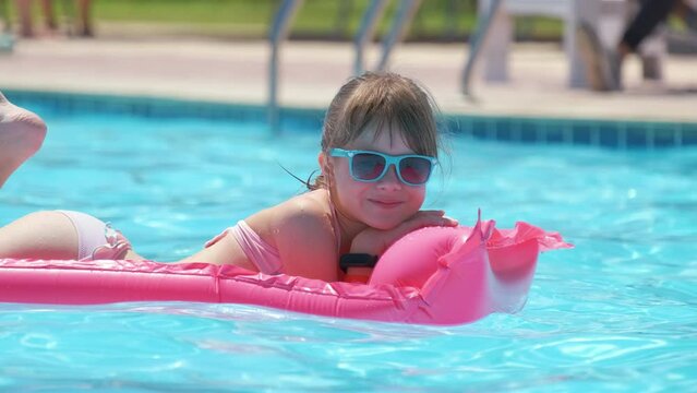Happy child girl relaxing on inflatable air mattress in swimming pool on sunny summer day during tropical vacations. Summertime activities concept