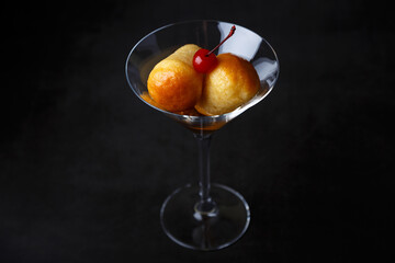 Neapolitan Rum baba (or baba au rum) in a martini glass with a cocktail cherry on a black...