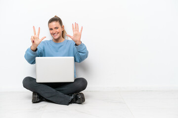 Young woman with a laptop sitting on the floor counting eight with fingers