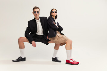 Full-length portrait of stylish young man and woman in retro suit posing isolated over grey studio...