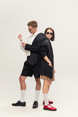 Full-length portrait of stylish young couple, man and woman standing in one jacket, posing isolated over grey studio background
