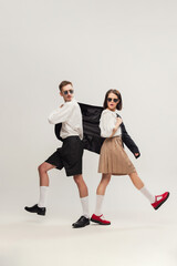 Full-length portrait of stylish young couple, man and woman in retro suit posing isolated over grey studio background