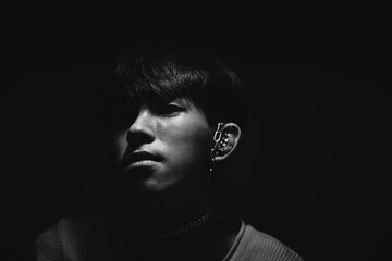 Black and white photo of Asian male black short-straight hair looking at camera with stainless earring and necklace. Abstract high low exposure contrast shadow.