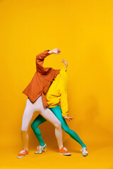 Creative colorful portrait of man and woman in bright clothes with hidden faces posing isolated over yellow background. Strange pose.