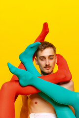 Creative colorful portrait of man with female legs in bright tights twining him isolated over yellow background. Extravagant.