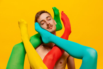 Creative colorful portrait of man with female legs in bright tights twining him isolated over yellow background. Extraordinary.