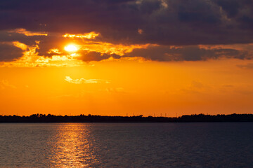 Beautiful colorful yellow orange blue sunset over the sea with sun reflections on the calm water surface and copy space on the clouds