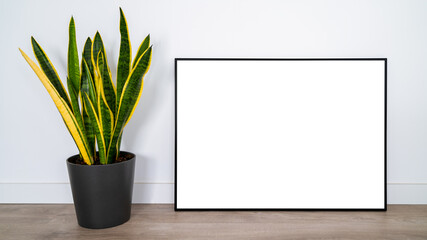 White poster on wood floor with black frame and plant mockup for you design.