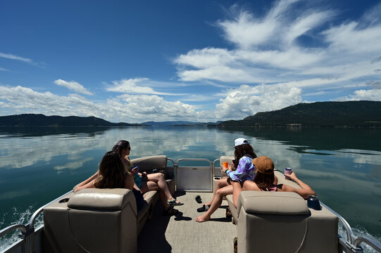 Four young women enjoying ride on pontoon boat on calm water of Flathead Lake, Montana on sunny summer morning.