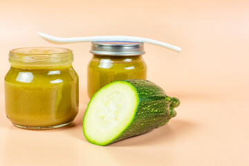 Baby food. Two glass jars with baby squash puree (zucchini) and a spoon on a beige background. Space for text.