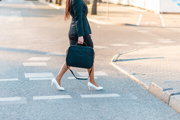 Legs detail of business woman on the way to office, walking outdoors holding a laptop case, wearing business suit and high heels.Cropped view of business woman walking in city.Copy space, waist down.