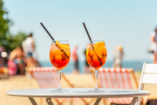 Two glasses of orange spritz aperol drink cocktail on table outdoors with sea and trees view blurred background.