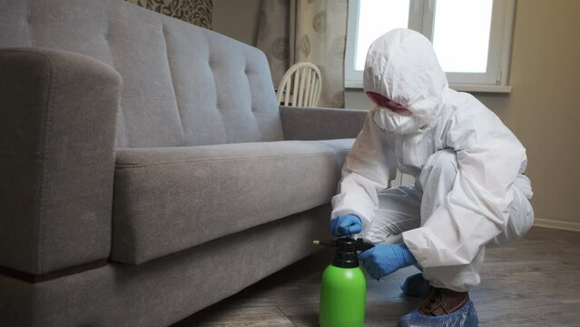 An exterminator in work clothes sprays pesticides with a spray gun. Fight against insects in apartments and houses. Disinsection of the premises