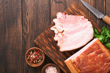 Whole Smoked Slab Bacon. Brisket. Sliced smoked gammon on a wooden table with rosemary, parsley,...