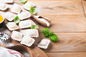 Obraz na płótnie Canvas Ravioli Italian food. Tasty homemade pasta ravioli with flour, tomatoes, eggs and greens basil on wooden background. Process of making italian ravioli. Food cooking ingredients background. Top view.